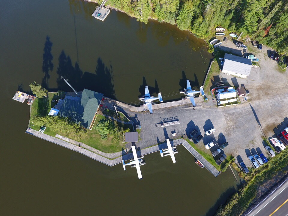 Aerial view of a seaplane dock with several planes parked on the water, surrounded by a lush green landscape and a small building nearby.