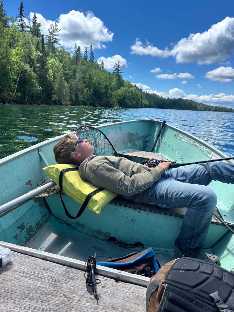 Angler asleep across the seats of a fishing boat, life jacket still on, during a Northwest Flying fly-in fishing trip, June 2026